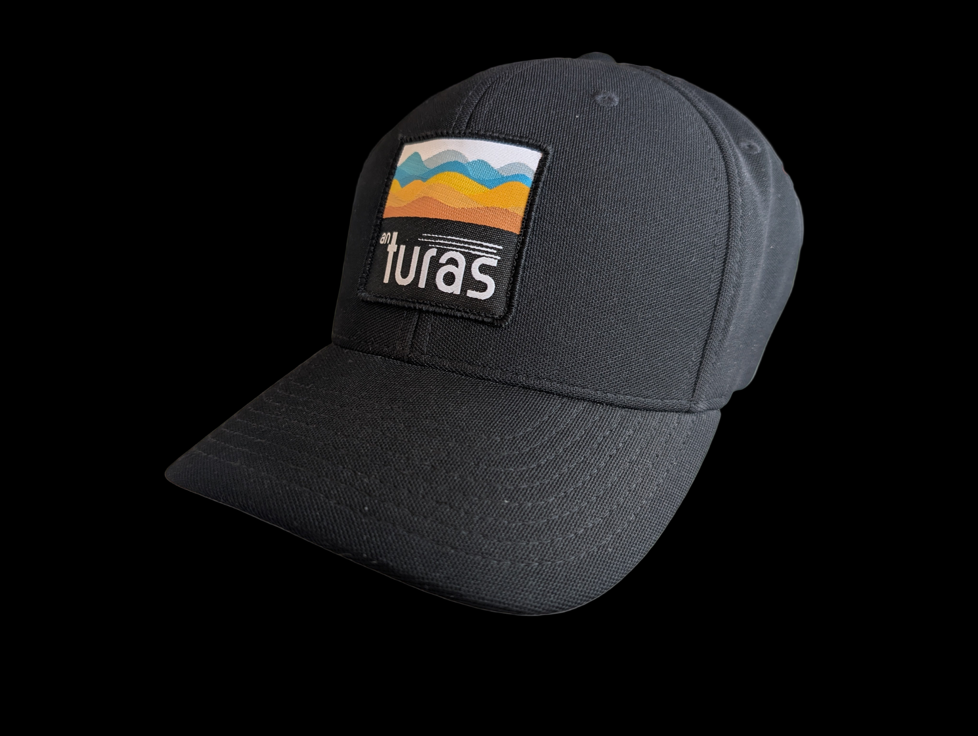 The Sòlas Cap. Black outdoor performance cap with a colorful landscape and An Turas™ logo on a woven patch.