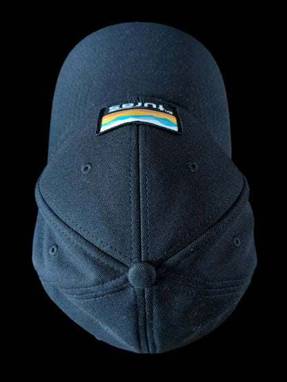 The Sòlas Cap. Black outdoor performance cap with a colorful landscape and An Turas™ logo on a woven patch. Aerial view.